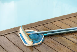 34269889 - wall brush and leaf skimmer maintenance tools on deck beside swimming pool
